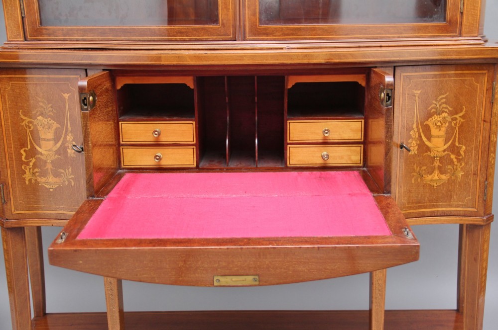 A 19th-century mahogany display cabinet featuring a upper bow-front section with two glazed doors, classical floral satinwood marquetry, a single central drawer, and tapered legs joined by a lower shelf. View VIII