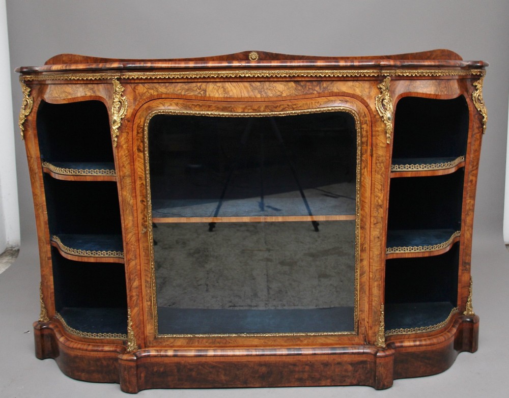 A 19th-century burr walnut credenza featuring a central glazed door, flanking curved open display shelves, and gilt ormolu mounts.
