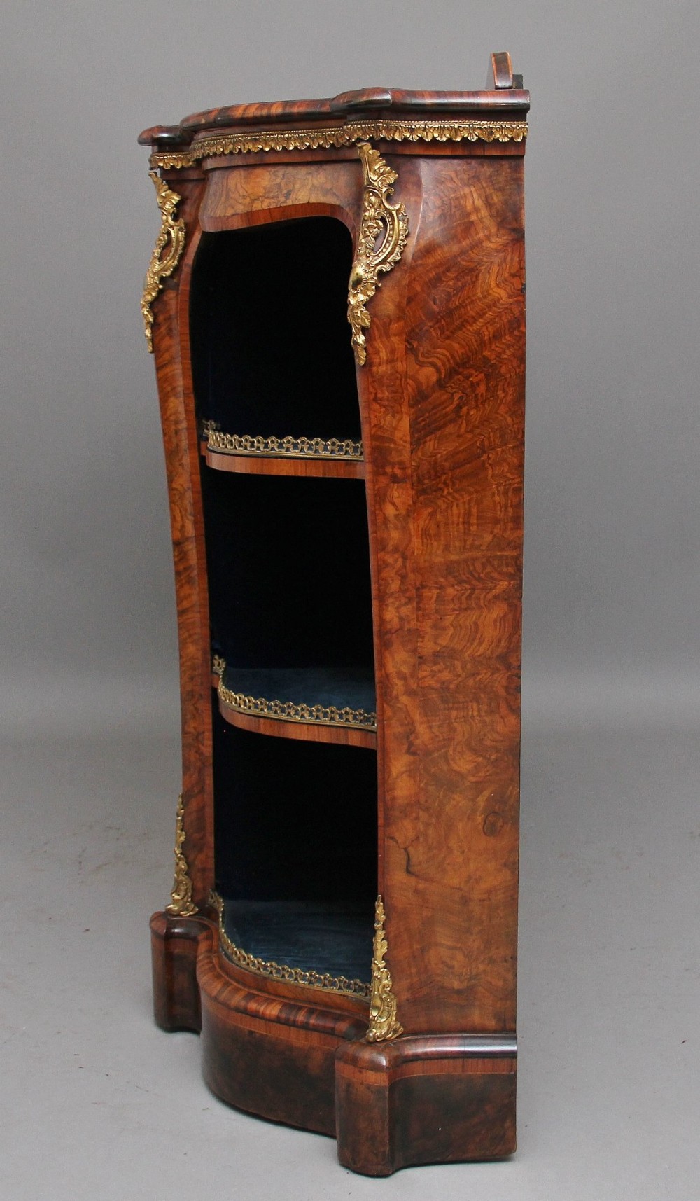 A 19th-century burr walnut credenza featuring a central glazed door, flanking curved open display shelves, and gilt ormolu mounts. View V