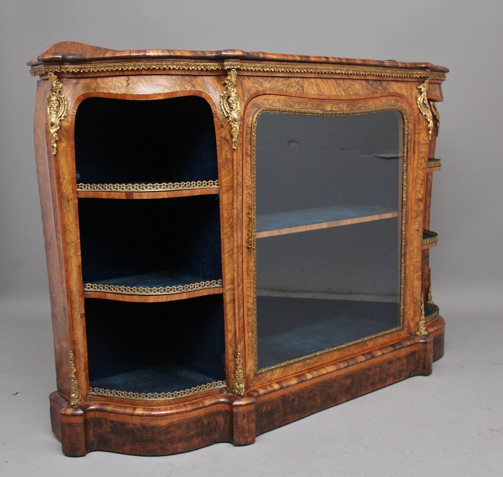 A 19th-century burr walnut credenza featuring a central glazed door, flanking curved open display shelves, and gilt ormolu mounts. View VIII