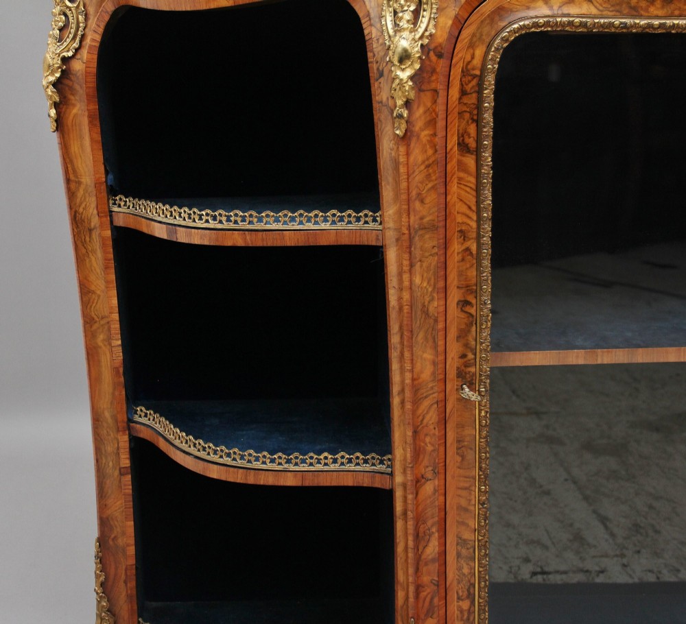 A 19th-century burr walnut credenza featuring a central glazed door, flanking curved open display shelves, and gilt ormolu mounts. View X