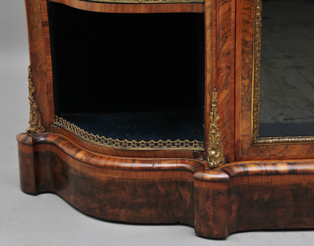 A 19th-century burr walnut credenza featuring a central glazed door, flanking curved open display shelves, and gilt ormolu mounts. View XII