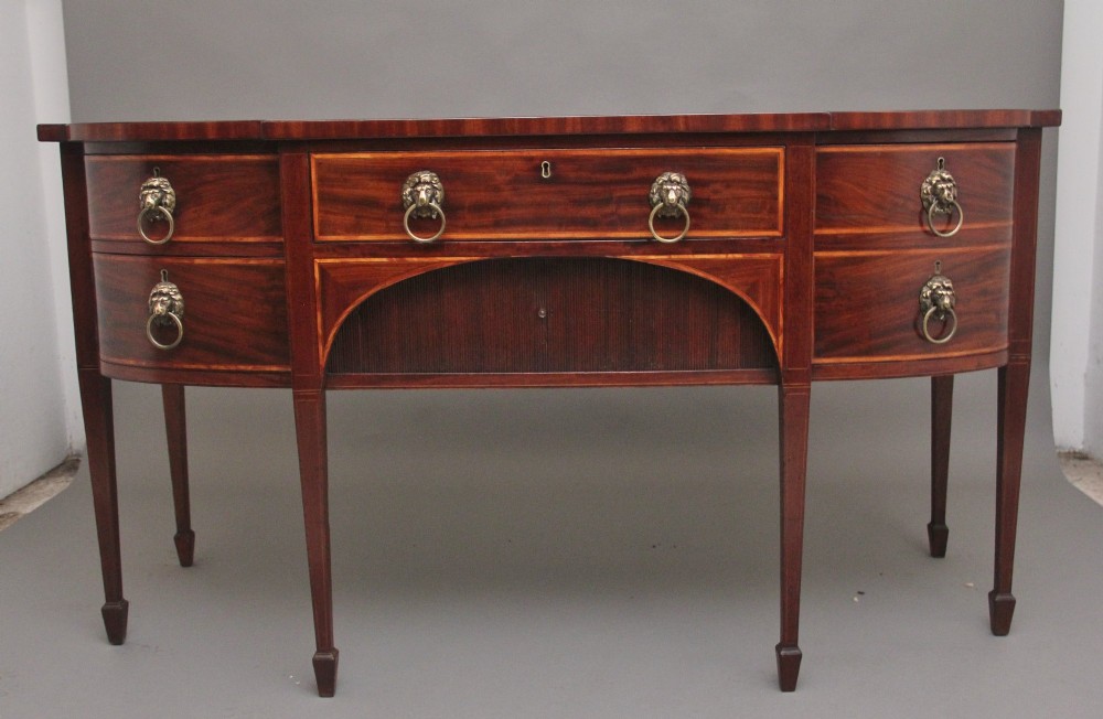 A nineteenth-century mahogany bowfront sideboard featuring inlaid crossbanding, multiple drawers with brass lion-mask ring handles, and tapered square legs.
