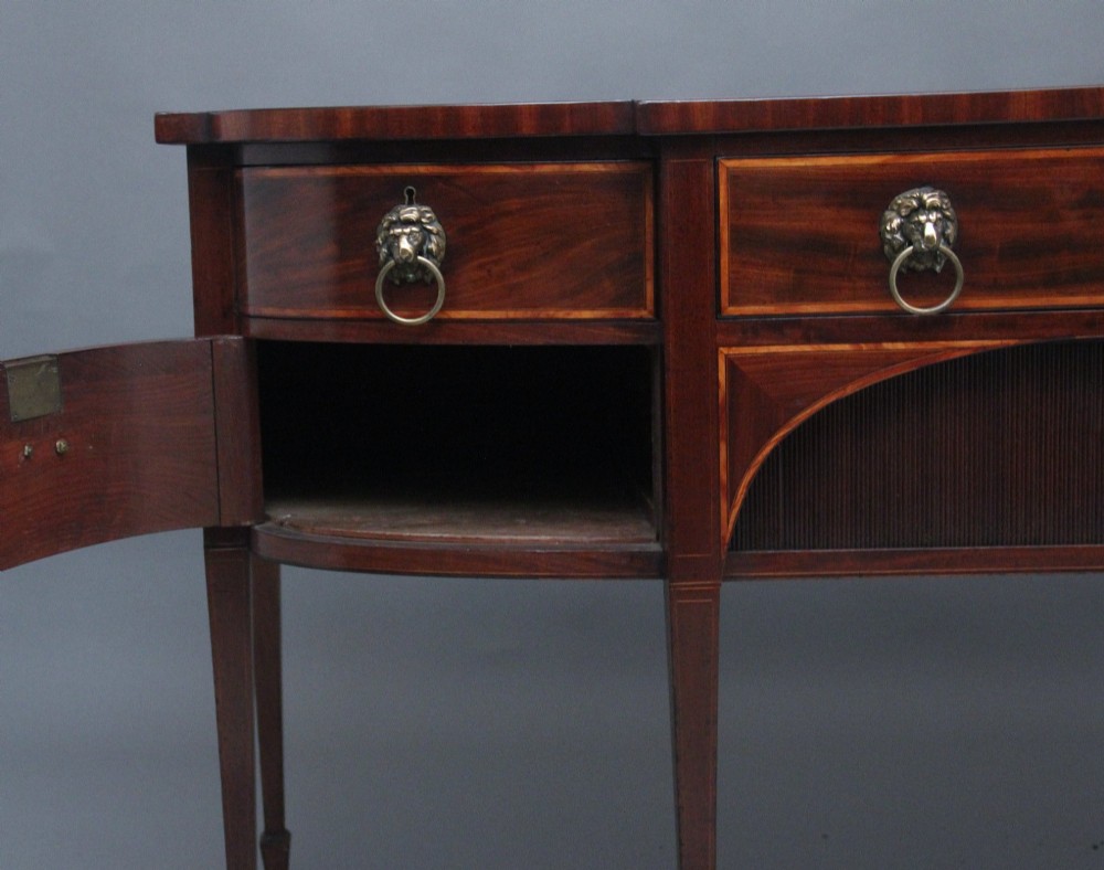 A nineteenth-century mahogany bowfront sideboard featuring inlaid crossbanding, multiple drawers with brass lion-mask ring handles, and tapered square legs. View III
