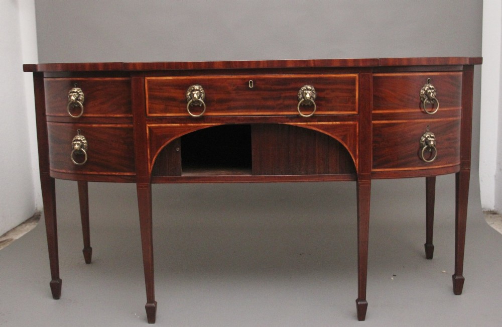 A nineteenth-century mahogany bowfront sideboard featuring inlaid crossbanding, multiple drawers with brass lion-mask ring handles, and tapered square legs. View IV