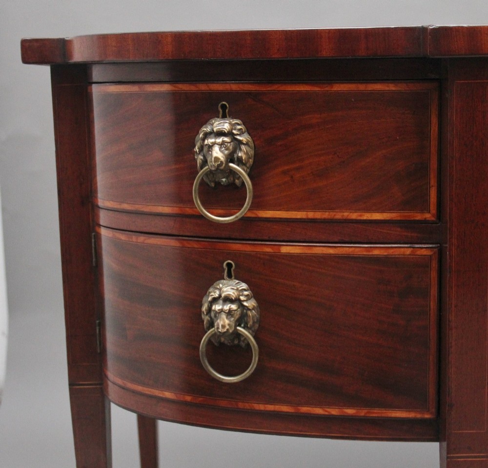 A nineteenth-century mahogany bowfront sideboard featuring inlaid crossbanding, multiple drawers with brass lion-mask ring handles, and tapered square legs. View VII