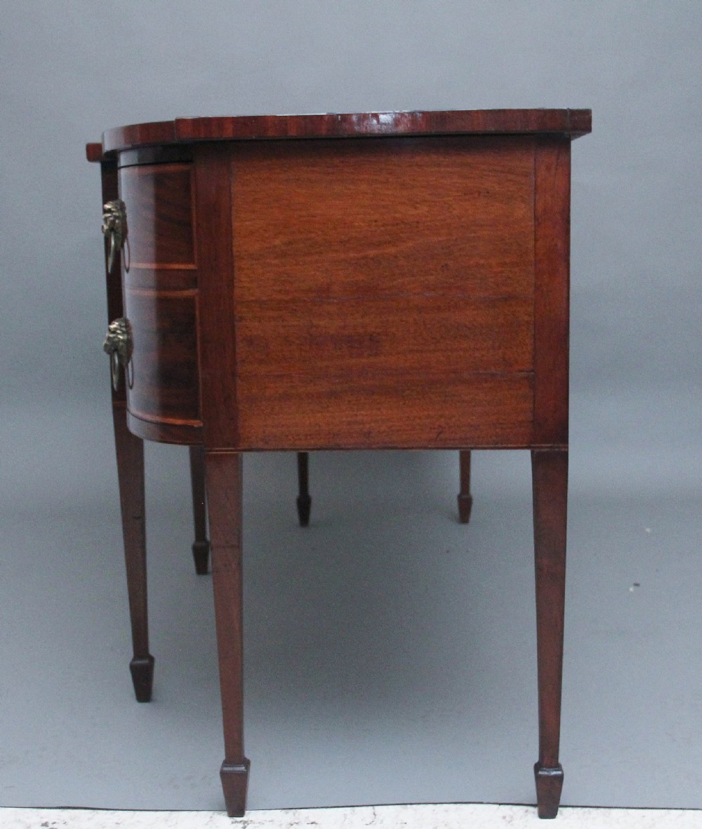 A nineteenth-century mahogany bowfront sideboard featuring inlaid crossbanding, multiple drawers with brass lion-mask ring handles, and tapered square legs. View XI