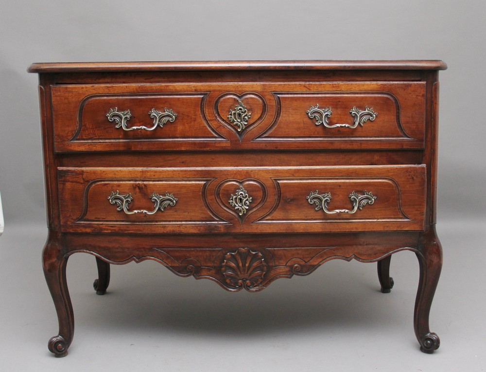 An early nineteenth-century French walnut commode featuring two deep drawers with carved heart-shaped escutcheon surrounds, decorative brass handles, a carved shell apron, and cabriole legs.