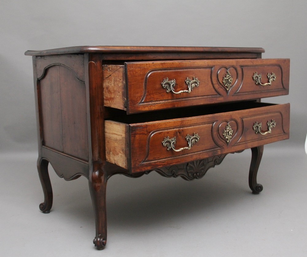 An early nineteenth-century French walnut commode featuring two deep drawers with carved heart-shaped escutcheon surrounds, decorative brass handles, a carved shell apron, and cabriole legs. View III