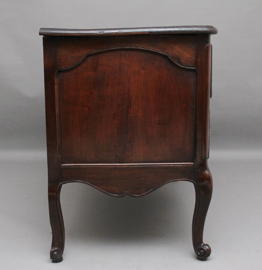 An early nineteenth-century French walnut commode featuring two deep drawers with carved heart-shaped escutcheon surrounds, decorative brass handles, a carved shell apron, and cabriole legs. View IV
