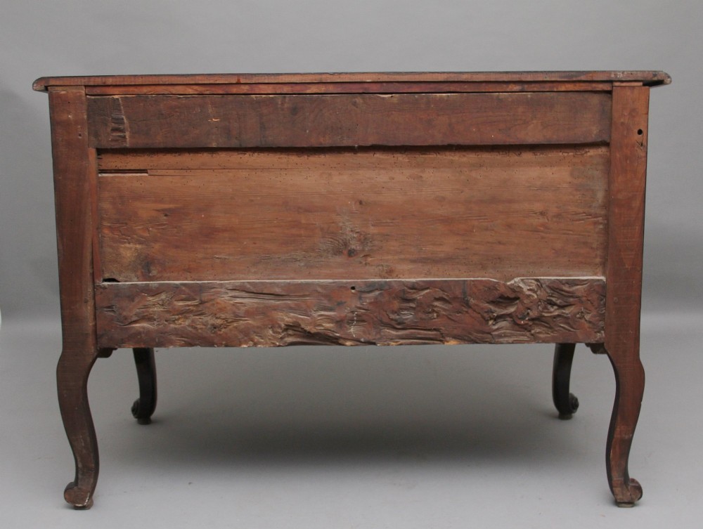 An early nineteenth-century French walnut commode featuring two deep drawers with carved heart-shaped escutcheon surrounds, decorative brass handles, a carved shell apron, and cabriole legs. View V