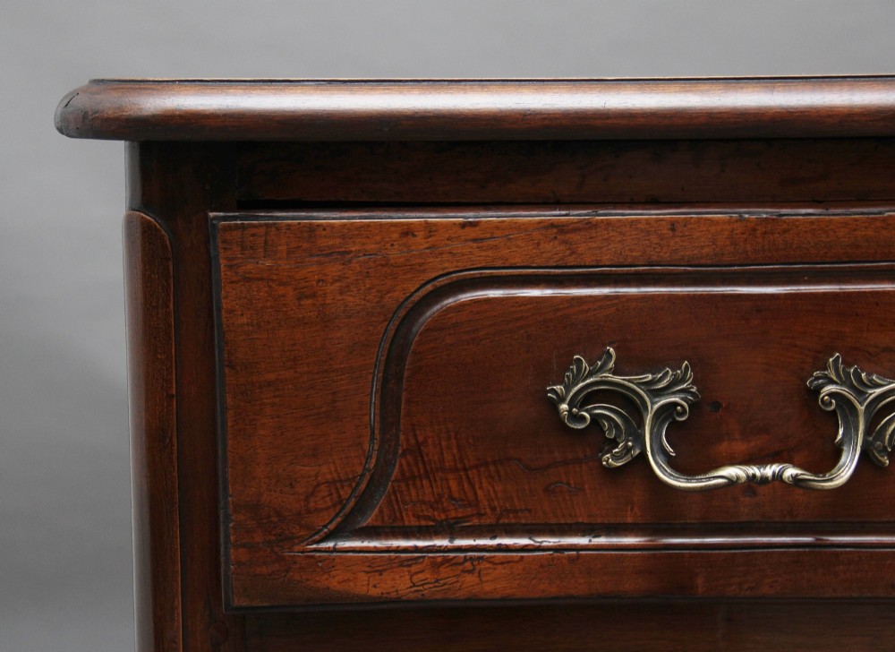 An early nineteenth-century French walnut commode featuring two deep drawers with carved heart-shaped escutcheon surrounds, decorative brass handles, a carved shell apron, and cabriole legs. View VIII