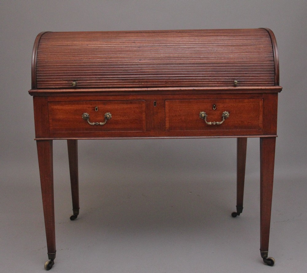 An early nineteenth-century mahogany tambour desk featuring a slatted roll-top cover, two drawers with brass handles, and square tapered legs on castors.