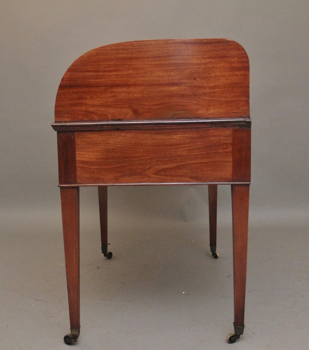 An early nineteenth-century mahogany tambour desk featuring a slatted roll-top cover, two drawers with brass handles, and square tapered legs on castors. View X