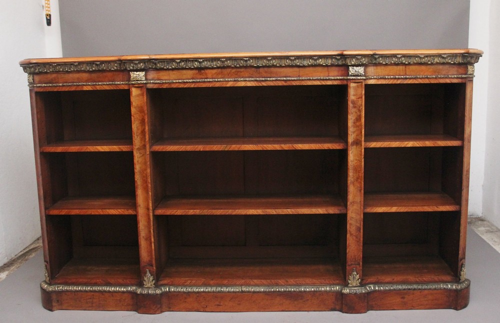 A nineteenth-century low open bookcase crafted from warm walnut wood featuring three sections with adjustable shelving and decorative gilt-bronze ormolu mounts along the borders.