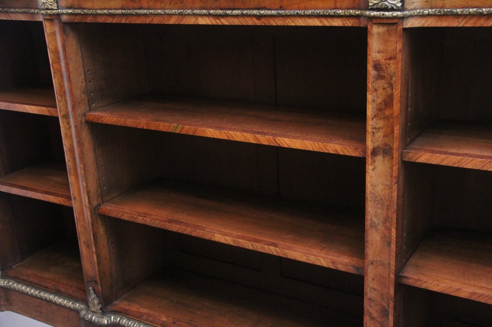 A nineteenth-century low open bookcase crafted from warm walnut wood featuring three sections with adjustable shelving and decorative gilt-bronze ormolu mounts along the borders. View V