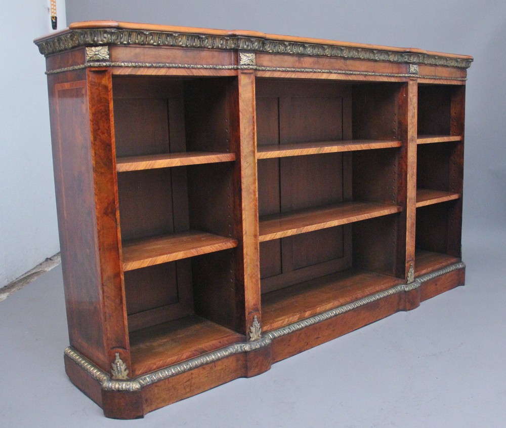 A nineteenth-century low open bookcase crafted from warm walnut wood featuring three sections with adjustable shelving and decorative gilt-bronze ormolu mounts along the borders. View X
