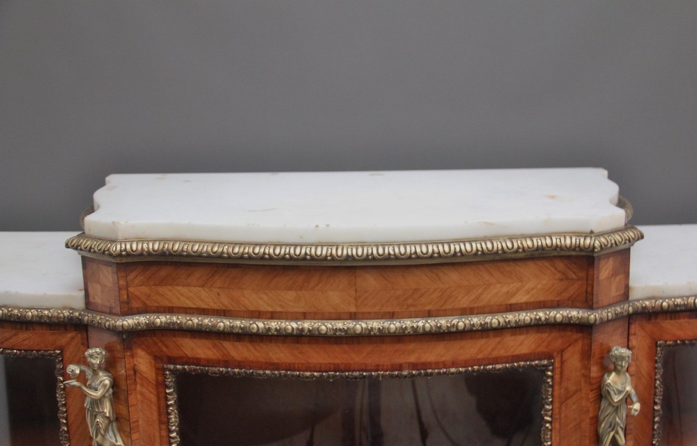 A 19th-century French kingwood credenza featuring a stepped white marble top, three glazed doors, parquetry veneer, and cast gilt-bronze caryatid mounts. View V