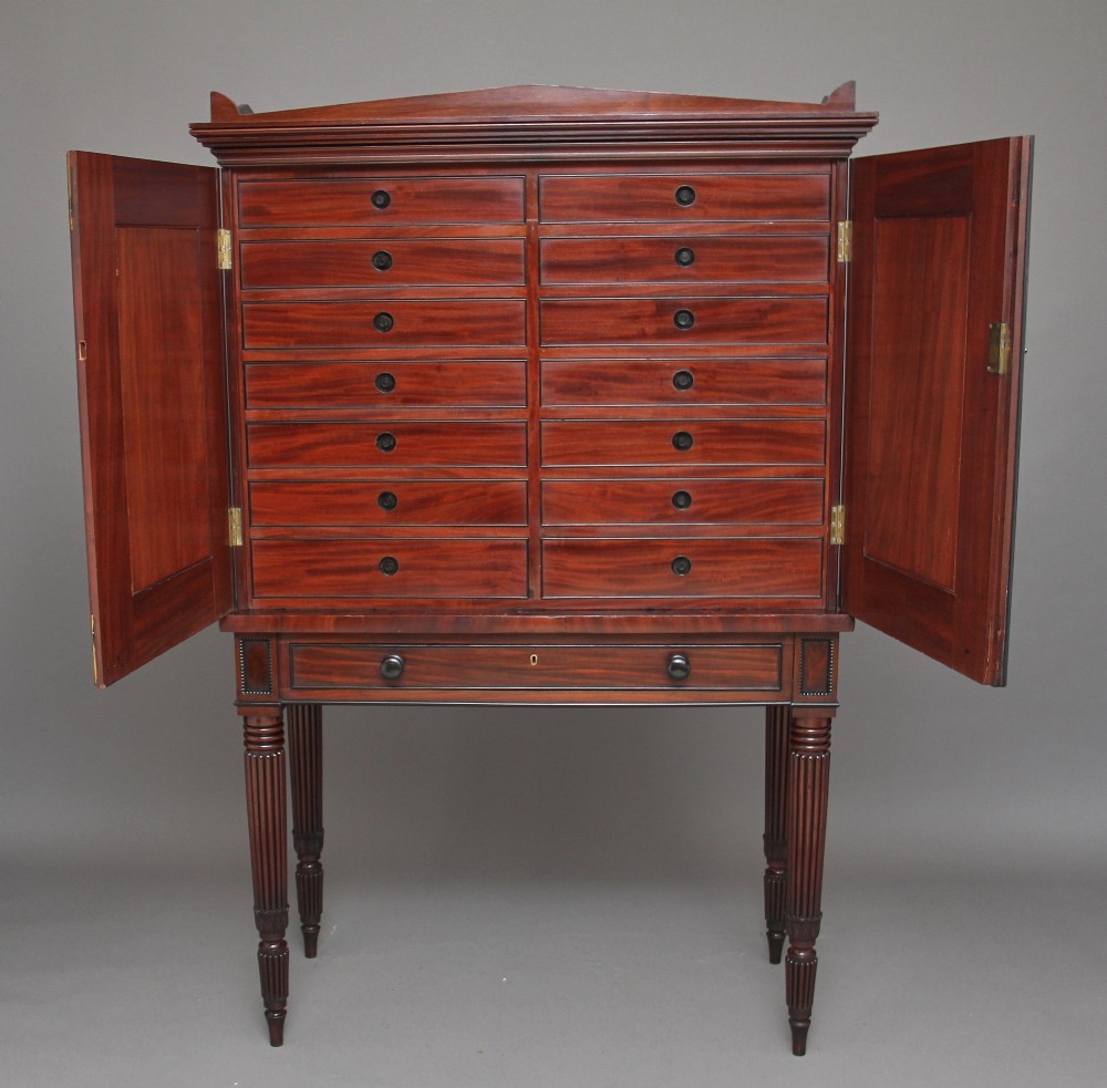 An early nineteenth-century mahogany cabinet on stand featuring flame-veneered panelled double doors above a drawer, supported by turned reeded legs. View III