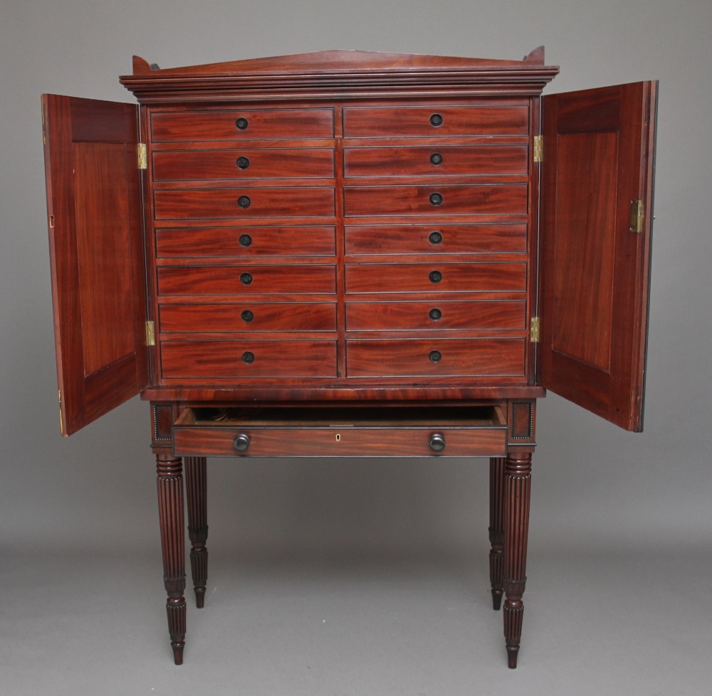 An early nineteenth-century mahogany cabinet on stand featuring flame-veneered panelled double doors above a drawer, supported by turned reeded legs. View IV