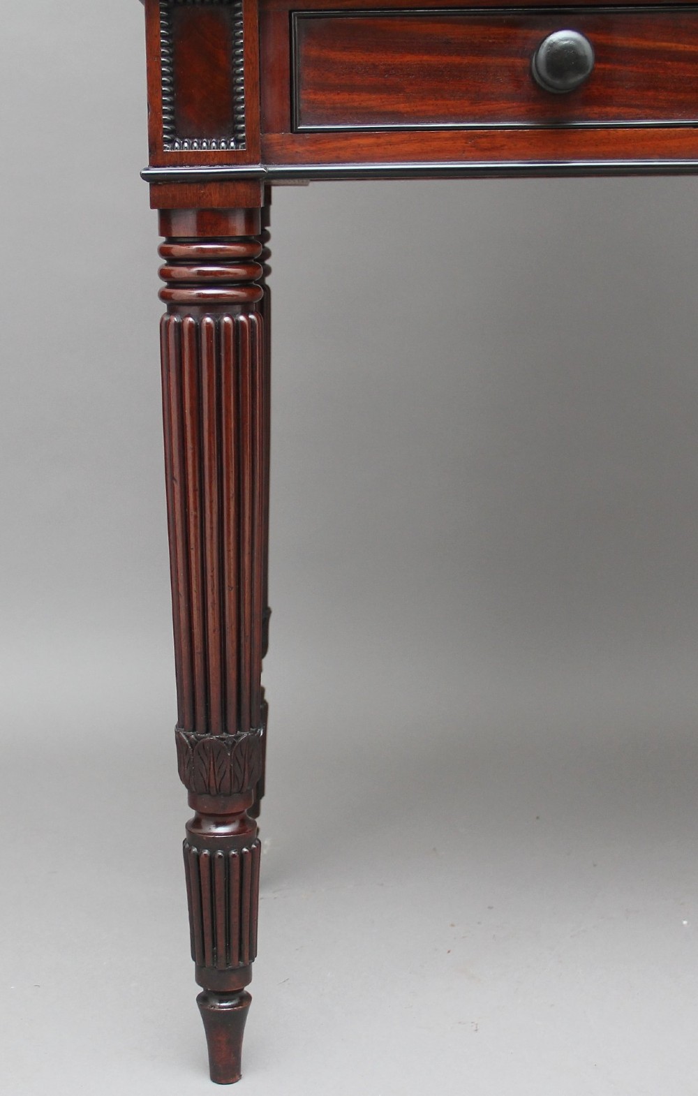 An early nineteenth-century mahogany cabinet on stand featuring flame-veneered panelled double doors above a drawer, supported by turned reeded legs. View V