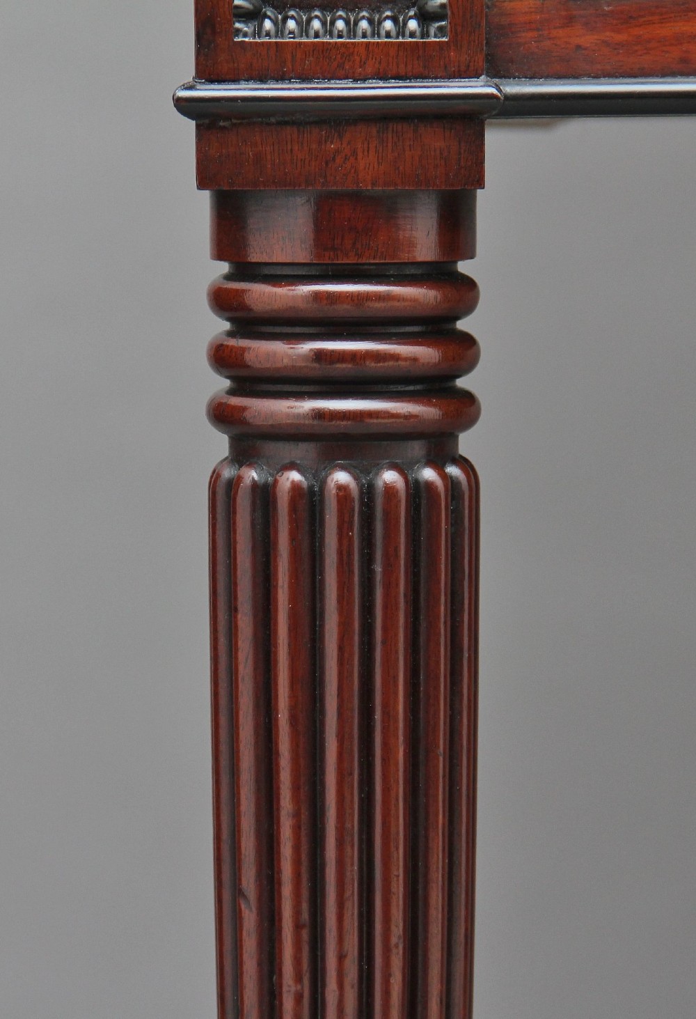 An early nineteenth-century mahogany cabinet on stand featuring flame-veneered panelled double doors above a drawer, supported by turned reeded legs. View VII
