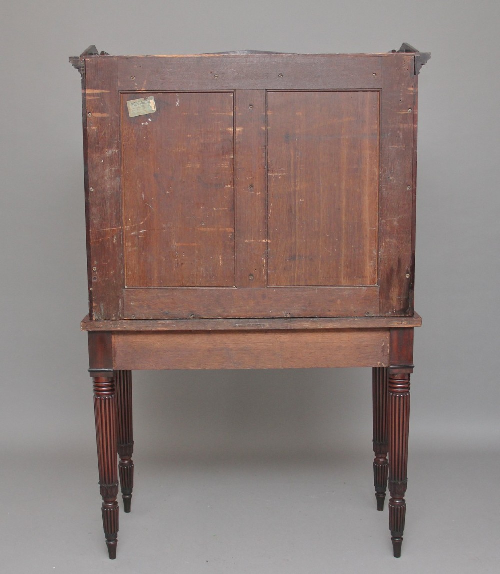 An early nineteenth-century mahogany cabinet on stand featuring flame-veneered panelled double doors above a drawer, supported by turned reeded legs. View XII