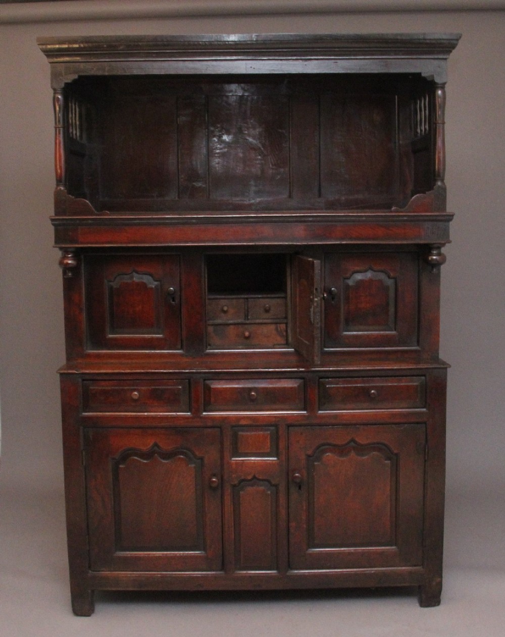 An early eighteenth-century dark Welsh oak tridarn featuring a three-tier design with an open top canopy, middle cupboards with arched panels, and a lower section with drawers and doors. View IV