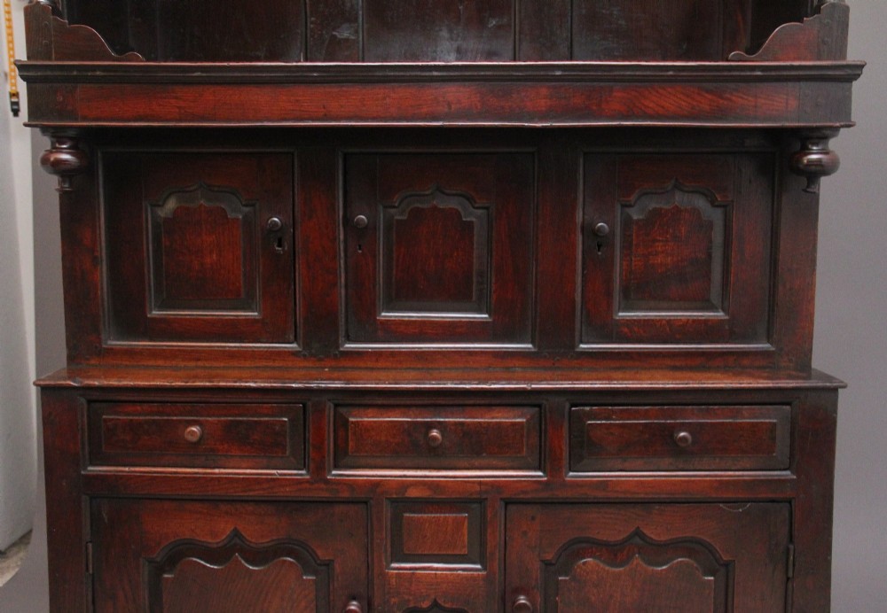 An early eighteenth-century dark Welsh oak tridarn featuring a three-tier design with an open top canopy, middle cupboards with arched panels, and a lower section with drawers and doors. View IX