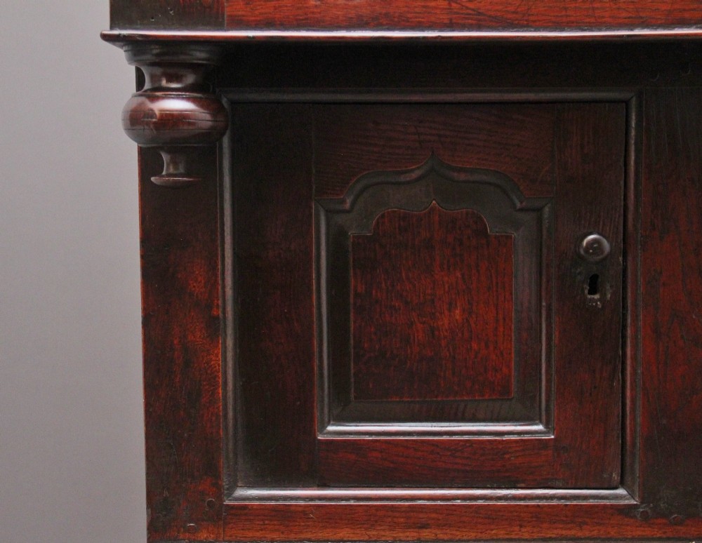 An early eighteenth-century dark Welsh oak tridarn featuring a three-tier design with an open top canopy, middle cupboards with arched panels, and a lower section with drawers and doors. View XI