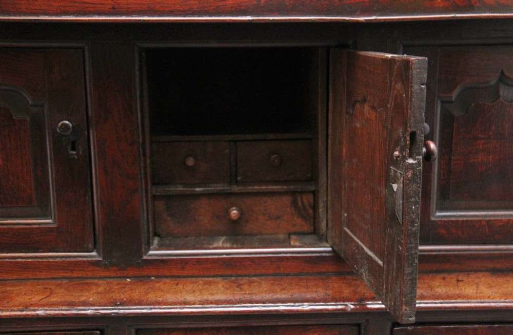 An early eighteenth-century dark Welsh oak tridarn featuring a three-tier design with an open top canopy, middle cupboards with arched panels, and a lower section with drawers and doors. View XIV