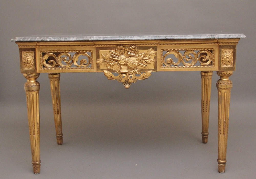 An 18th century Italian giltwood console table featuring an intricate carved frieze, fluted tapered legs, and a grey marble top.