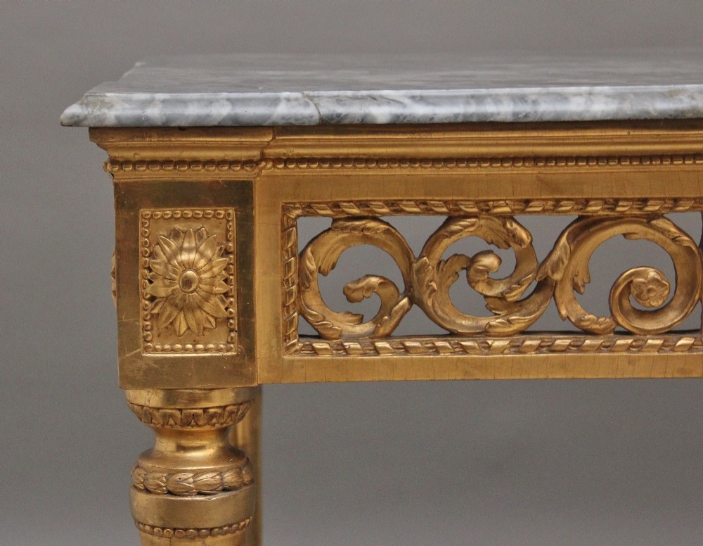 An 18th century Italian giltwood console table featuring an intricate carved frieze, fluted tapered legs, and a grey marble top. View II