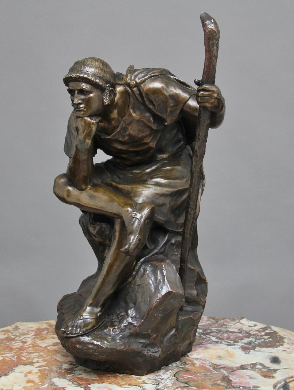 A 19th-century patinated bronze sculpture depicting the mythological figure Oedipus seated on a rock in contemplation while holding a staff. View III
