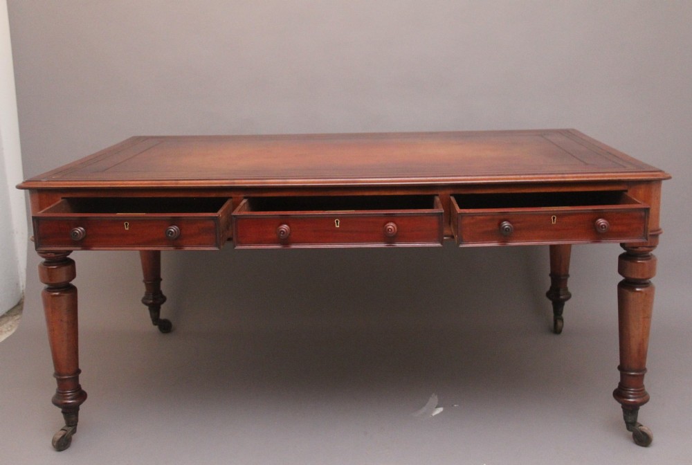 A 19th-century mahogany partners writing table featuring three drawers with turned wooden knobs, an inset leather surface, and four turned legs on brass castors. View II