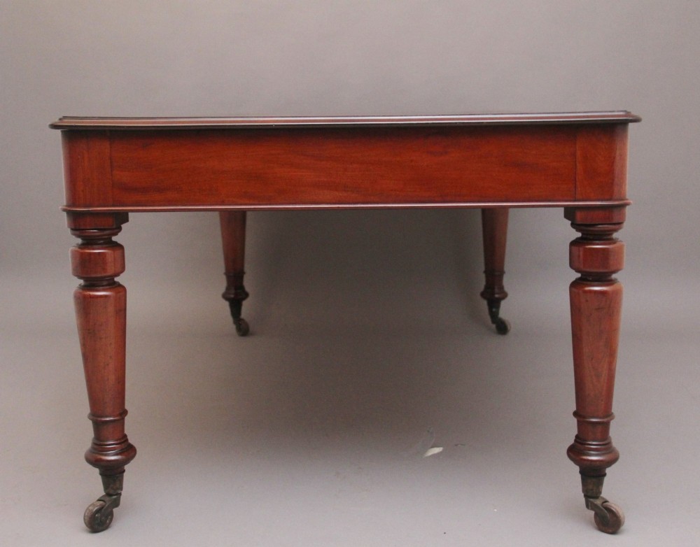 A 19th-century mahogany partners writing table featuring three drawers with turned wooden knobs, an inset leather surface, and four turned legs on brass castors. View V