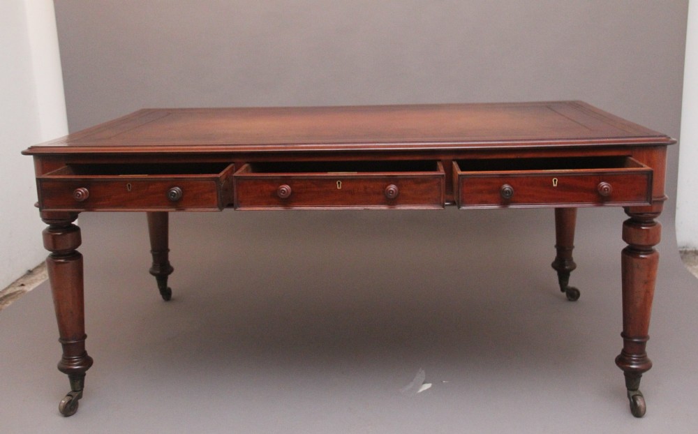 A 19th-century mahogany partners writing table featuring three drawers with turned wooden knobs, an inset leather surface, and four turned legs on brass castors. View VII