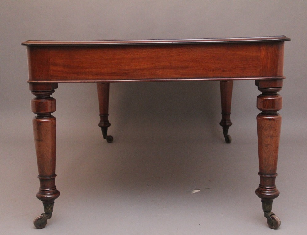 A 19th-century mahogany partners writing table featuring three drawers with turned wooden knobs, an inset leather surface, and four turned legs on brass castors. View VIII
