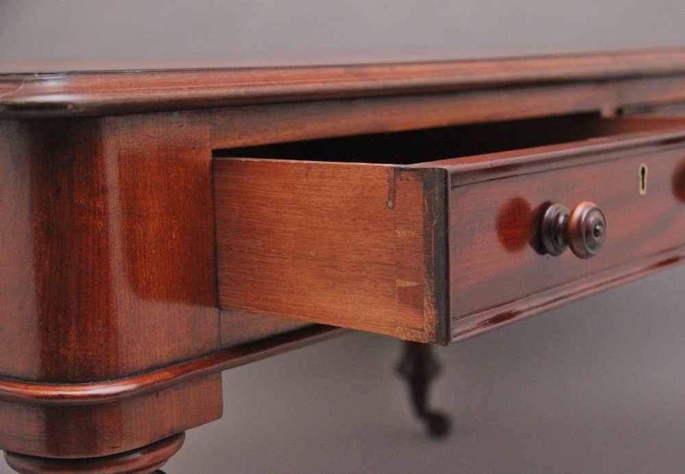 A 19th-century mahogany partners writing table featuring three drawers with turned wooden knobs, an inset leather surface, and four turned legs on brass castors. View X