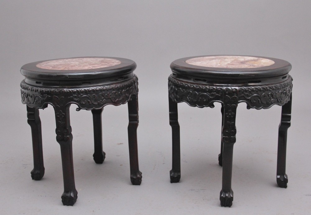 A pair of 19th-century Chinese carved dark hardwood circular occasional tables with inset pink marble tops and carved legs.