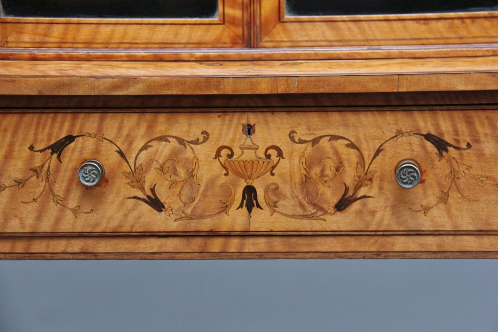 A 19th-century satinwood display cabinet featuring central glazed double doors, curved side shelves, a marquetry-inlaid drawer, and slender tapered legs with a lower undertier. View VIII