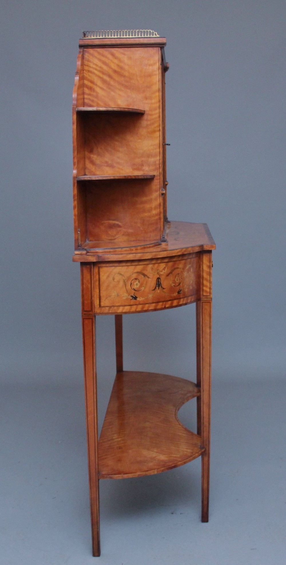 A 19th-century satinwood display cabinet featuring central glazed double doors, curved side shelves, a marquetry-inlaid drawer, and slender tapered legs with a lower undertier. View IX