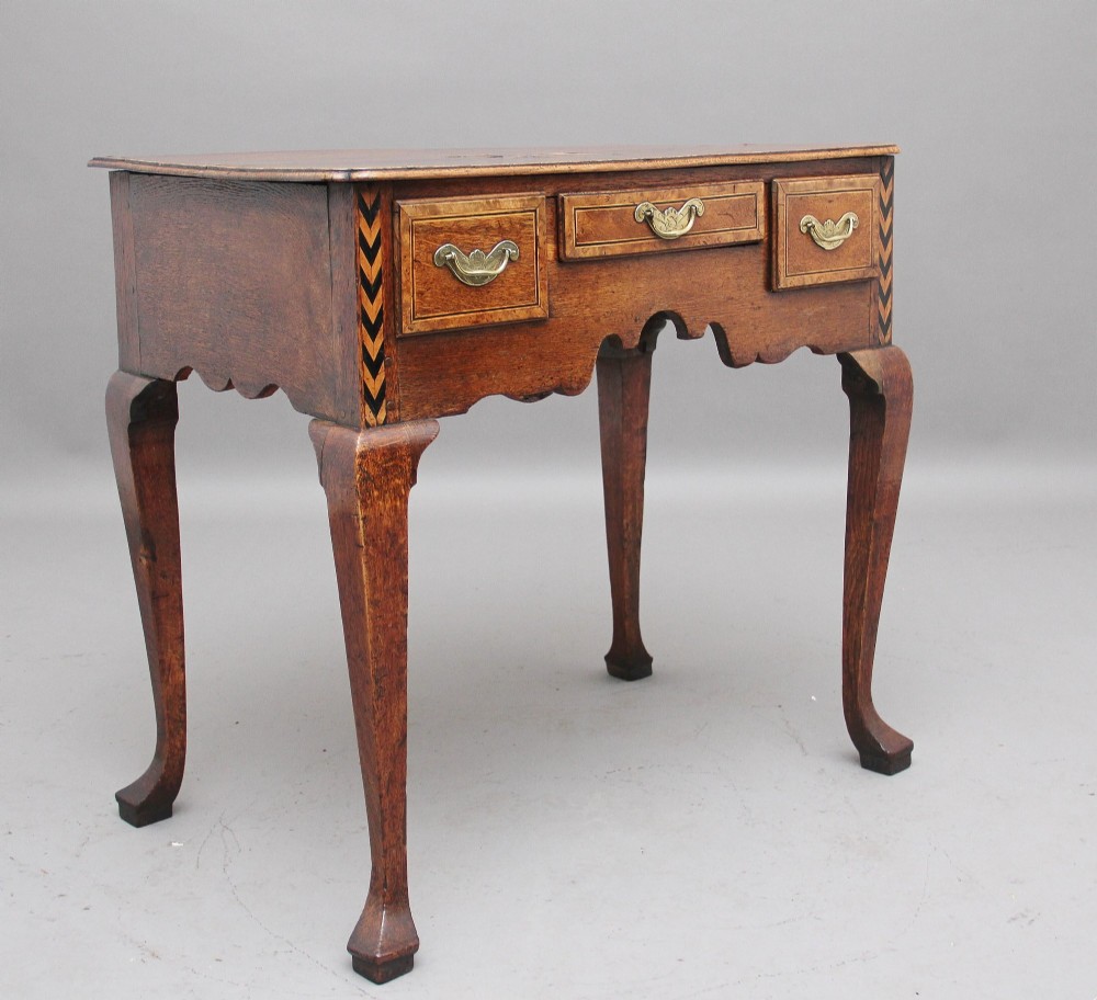 An 18th-century oak lowboy table featuring three drawers with brass handles, inlaid chevron borders, a scalloped apron, and four cabriole legs. View II