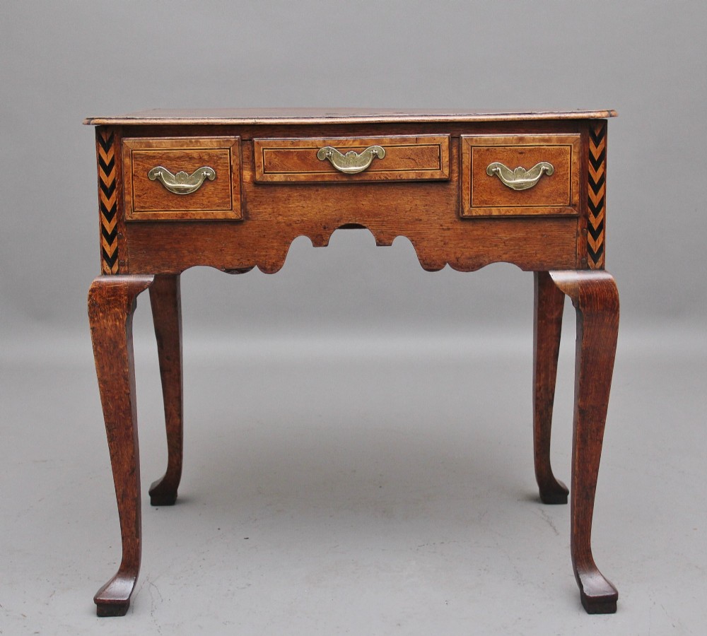 An 18th-century oak lowboy table featuring three drawers with brass handles, inlaid chevron borders, a scalloped apron, and four cabriole legs. View IV