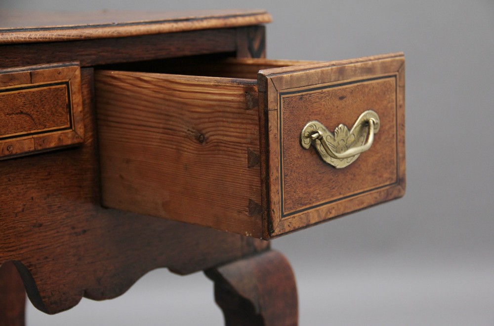 An 18th-century oak lowboy table featuring three drawers with brass handles, inlaid chevron borders, a scalloped apron, and four cabriole legs. View X