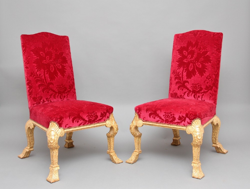 A pair of George I style giltwood side chairs featuring carved mask motifs on the legs and upholstered in rich red patterned velvet.
