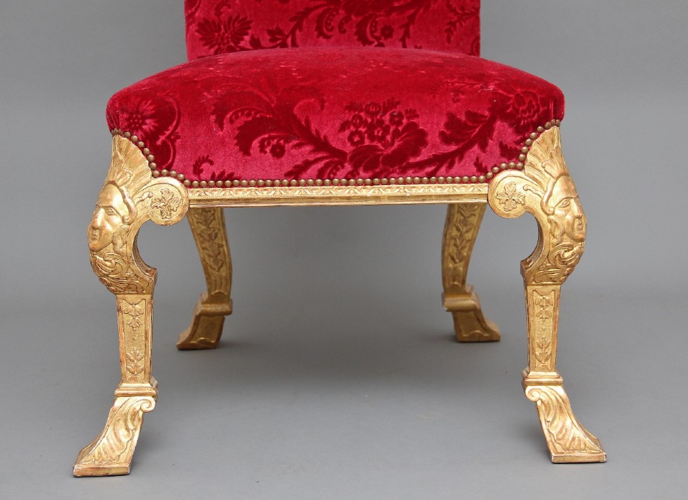 A pair of George I style giltwood side chairs featuring carved mask motifs on the legs and upholstered in rich red patterned velvet. View V