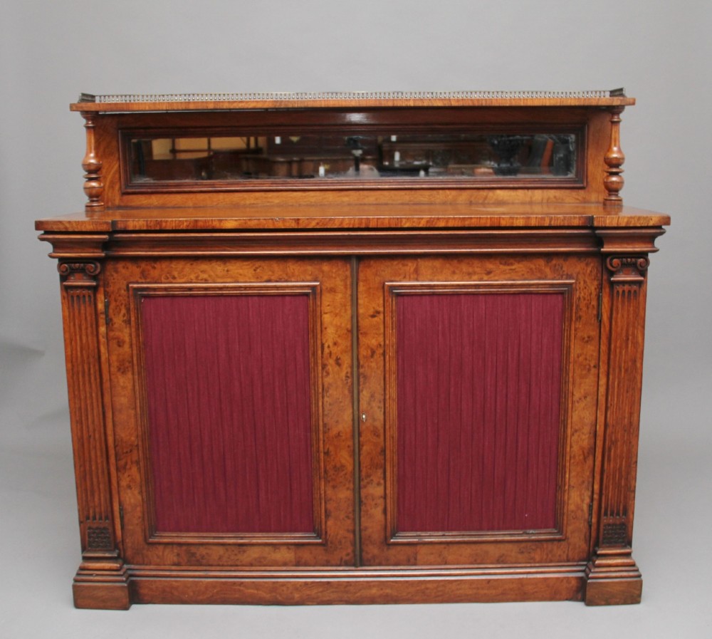 A nineteenth-century pollard oak cabinet featuring a mirrored gallery top, fluted column pillars, and twin doors with fabric-lined panels.