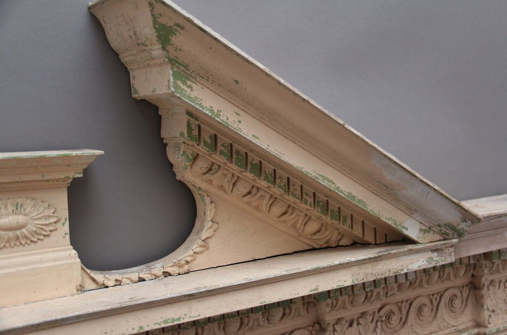 An 18th-century carved pine architectural overmantel featuring a broken pediment, fluted pilasters, dentil mouldings, and a central circular aperture in distressed off-white paint. View IV