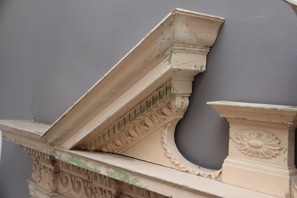 An 18th-century carved pine architectural overmantel featuring a broken pediment, fluted pilasters, dentil mouldings, and a central circular aperture in distressed off-white paint. View V